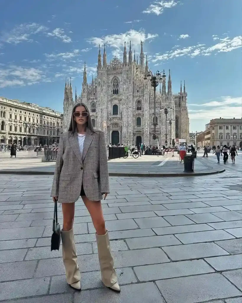 Fashionable woman in a plaid blazer and knee-high boots poses in front of Milan's stunning Duomo Cathedral.