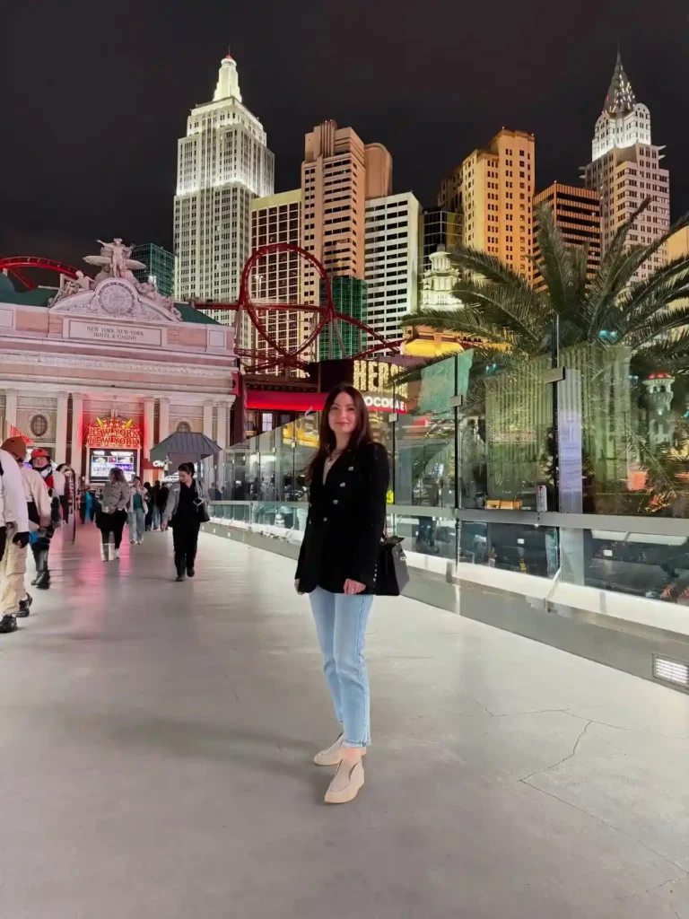 A woman stands on a vibrant Las Vegas street, surrounded by iconic skyscrapers and illuminated attractions at night.