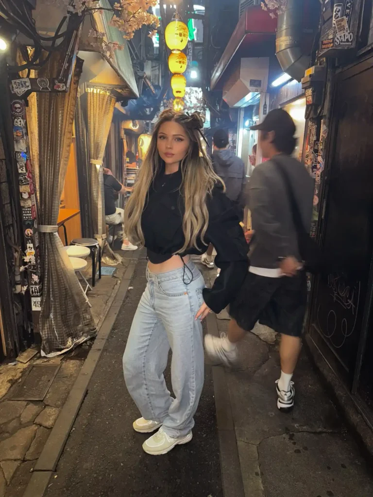 A stylish person poses in a bustling alley adorned with lanterns and street art, showcasing vibrant city life.