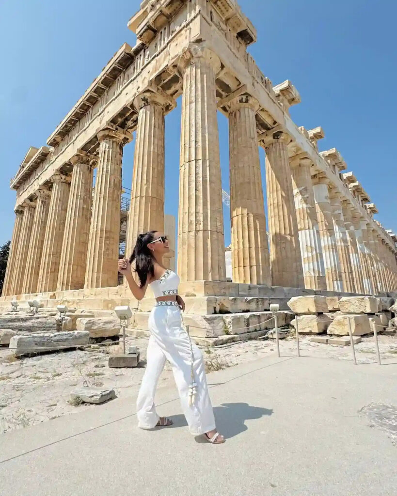 Woman in stylish outfit walking among the ancient columns of the Parthenon in Athens, Greece on a clear sunny day.