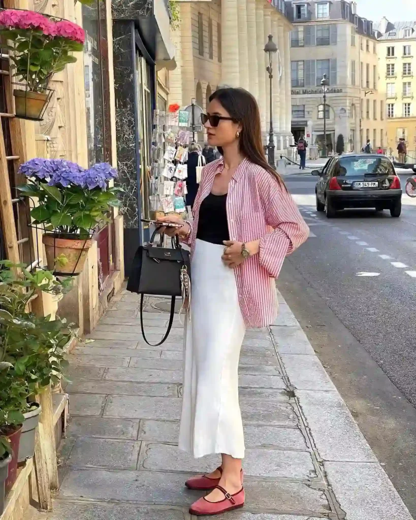 Young woman in stylish outfit shopping near flower shop on a sunny street with vibrant hydrangeas in Paris.