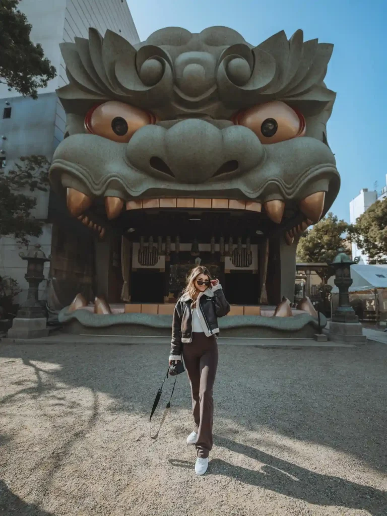 A woman poses in front of a large, sculpted lion head entrance, showcasing a unique architectural landmark.
