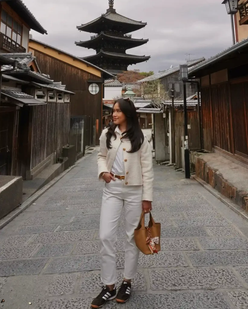 A woman in stylish attire walks down a historic street in Kyoto, with a pagoda in the background.