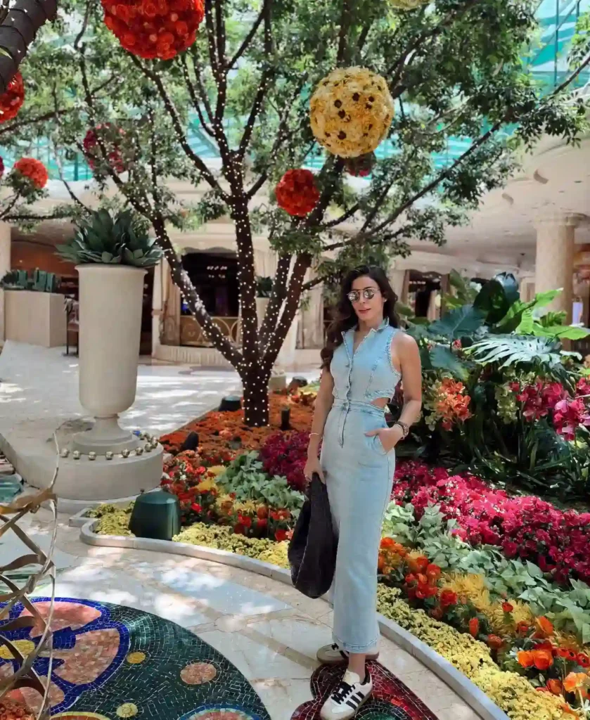 Young woman in a stylish denim jumpsuit stands among vibrant floral displays in a beautifully decorated indoor space.