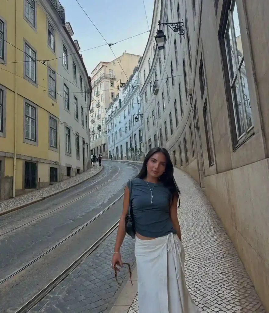 Woman in a stylish outfit posing on a curved cobblestone street lined with colorful buildings in Lisbon.