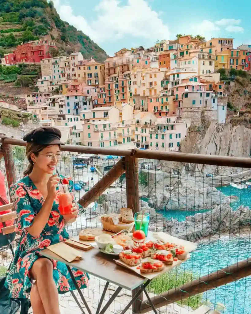 Enjoying a meal with colorful coastal views in Cinque Terre, Italy, featuring refreshing drinks and vibrant dishes.