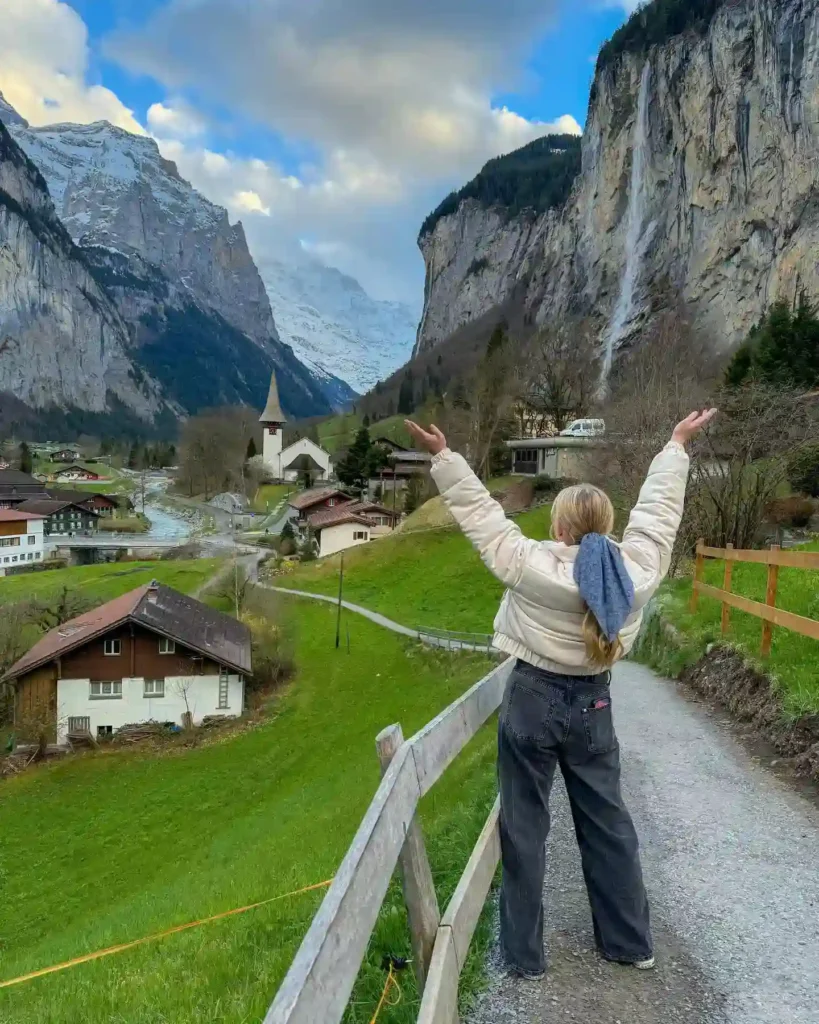 A person with outstretched arms enjoying the stunning mountain scenery in a picturesque alpine village.