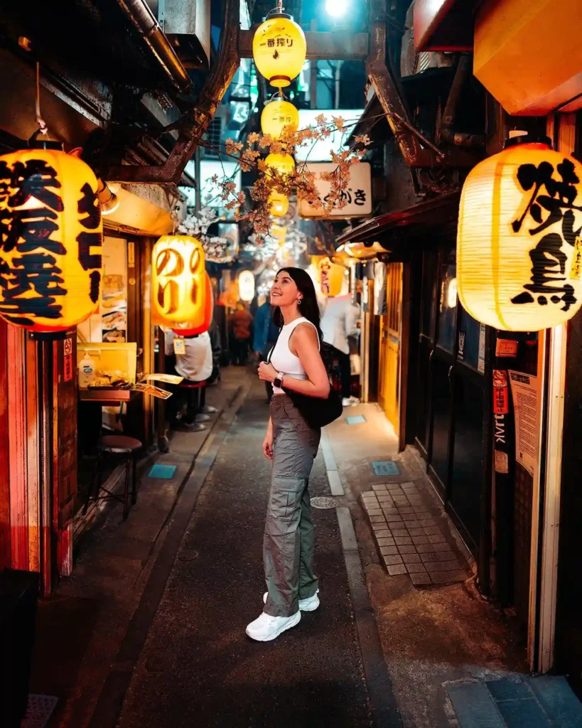 A woman explores a vibrant alley illuminated by glowing lanterns, capturing the essence of Japanese nightlife.