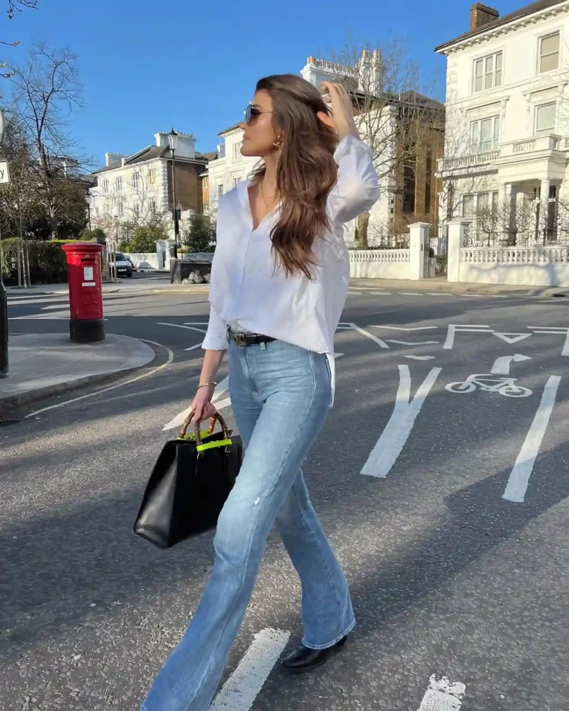 Woman in stylish outfit walking on a sunny street, holding a black handbag with a pop of color.