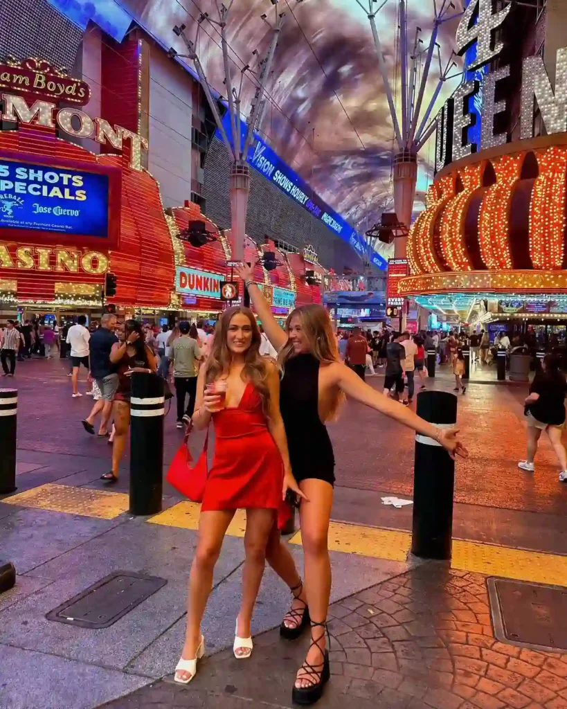 Two friends posing in vibrant outfits on Fremont Street, Las Vegas, with bright lights and a lively crowd in the background.
