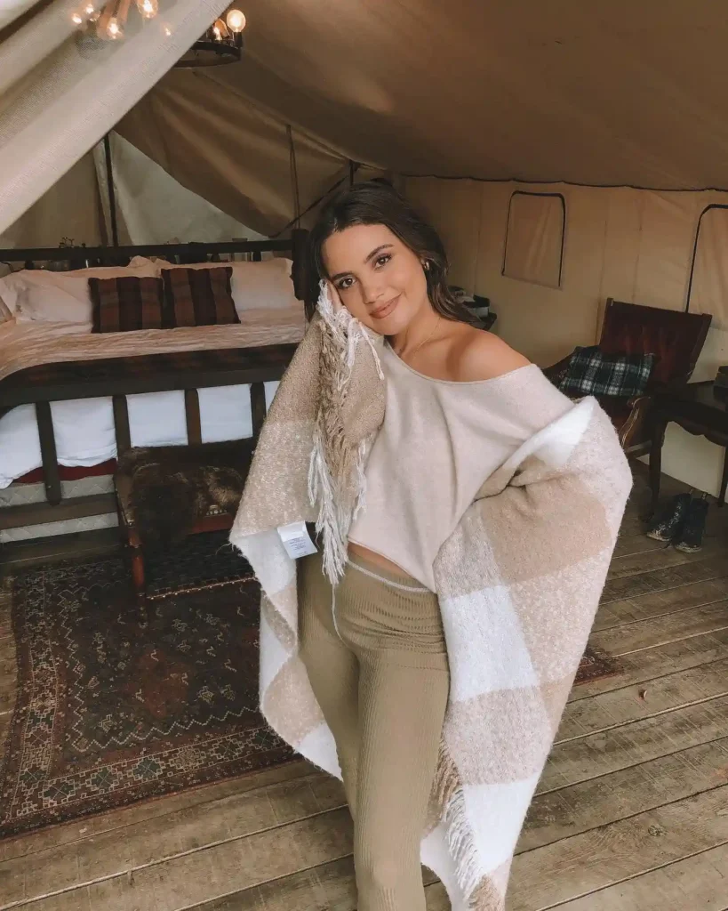 Cozy indoor scene with a woman wrapped in a blanket, styled in casual autumn fashion, exuding warmth and comfort.