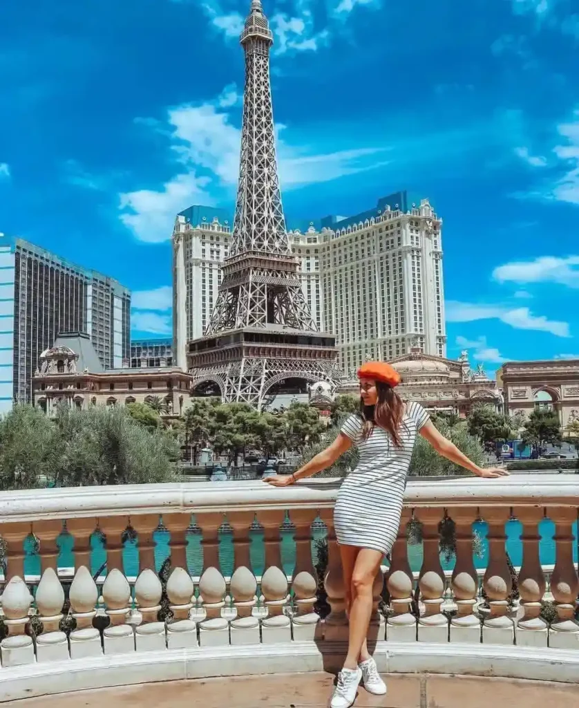 Young woman in a striped dress and orange beret poses in front of the Eiffel Tower replica in Las Vegas. Sunny day.