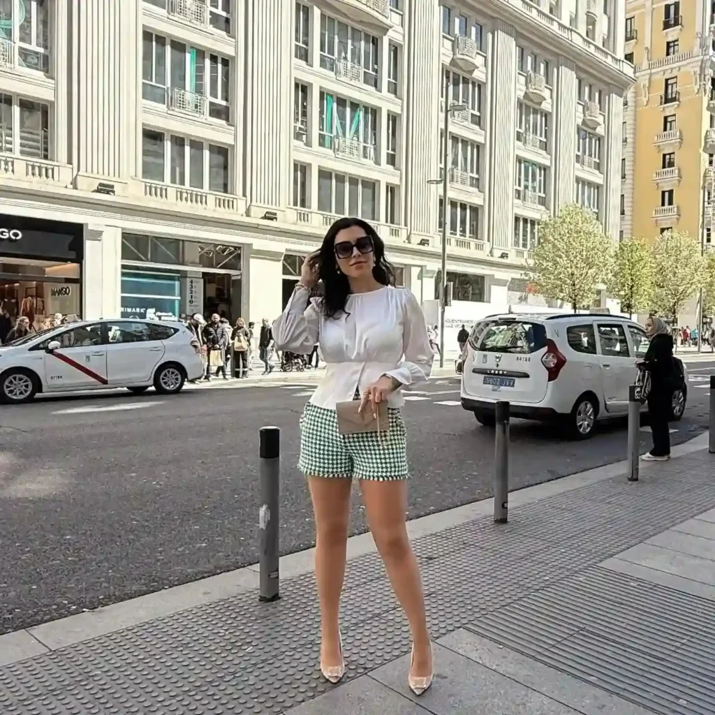 Fashionable woman in a stylish outfit stands on a city street, showcasing trendy summer attire against urban backdrop.