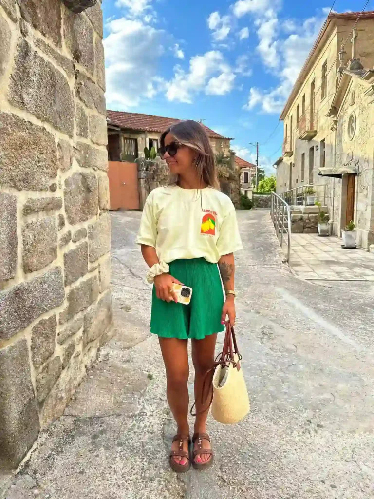 Young woman in trendy outfit standing on a charming street, enjoying a sunny day with clouds above.