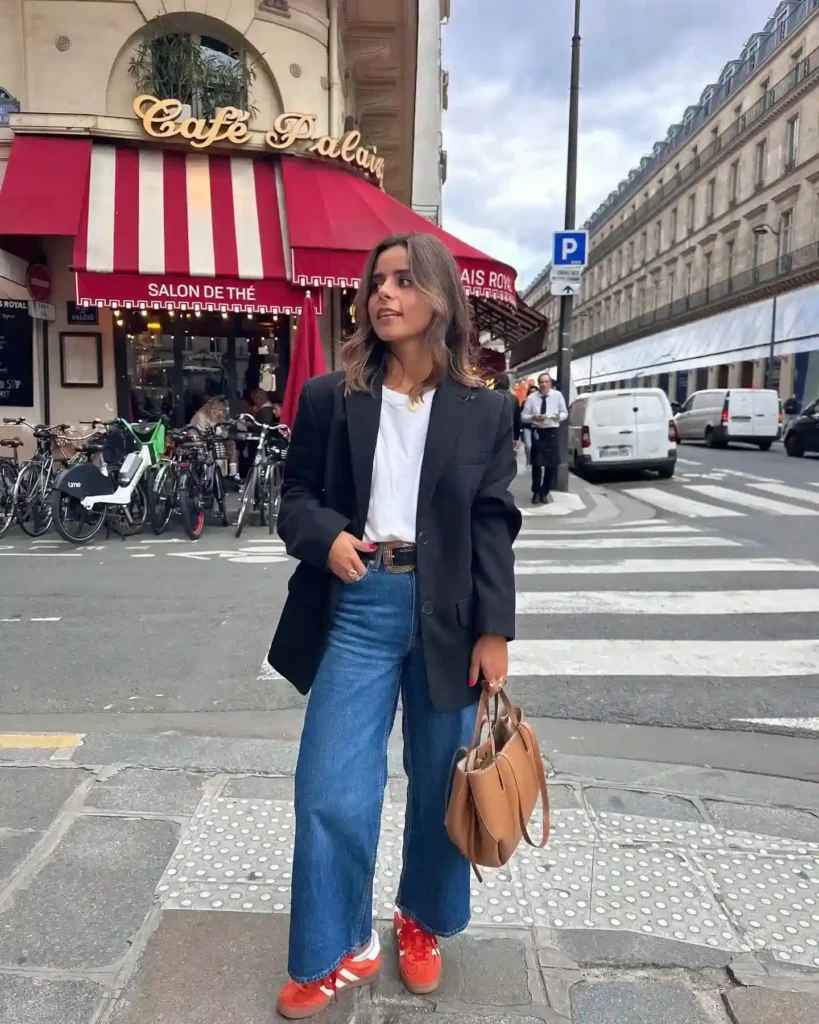 Woman in a chic outfit with a blazer and wide-leg jeans stands near Café Palais in Paris, showcasing a trendy street style.