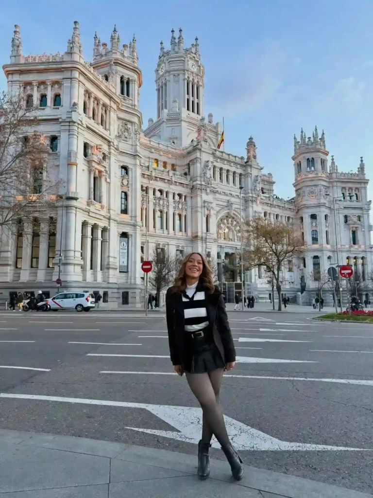Woman standing in front of a grand historic building, showcasing elegant architecture against a clear sky.