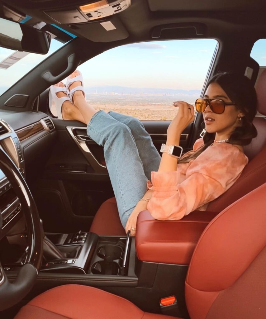 Young woman in stylish outfit relaxes in a luxurious car, enjoying scenic views with feet on the window.