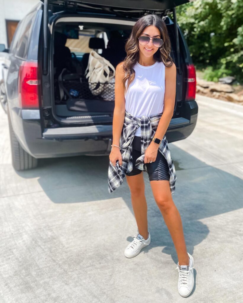 Young woman in casual outfit with sunglasses, standing by an open black SUV, ready for an adventurous day outdoors.