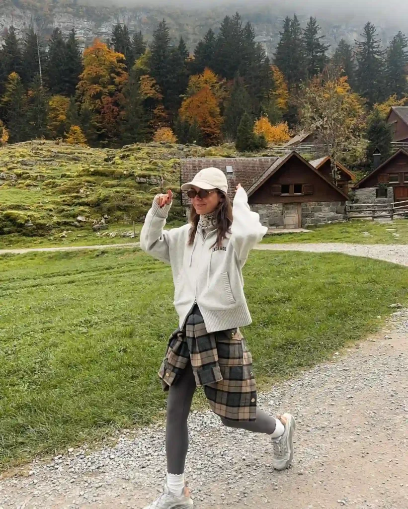 Young woman in casual outfit enjoying nature in autumn with colorful trees and charming cabins in the background.