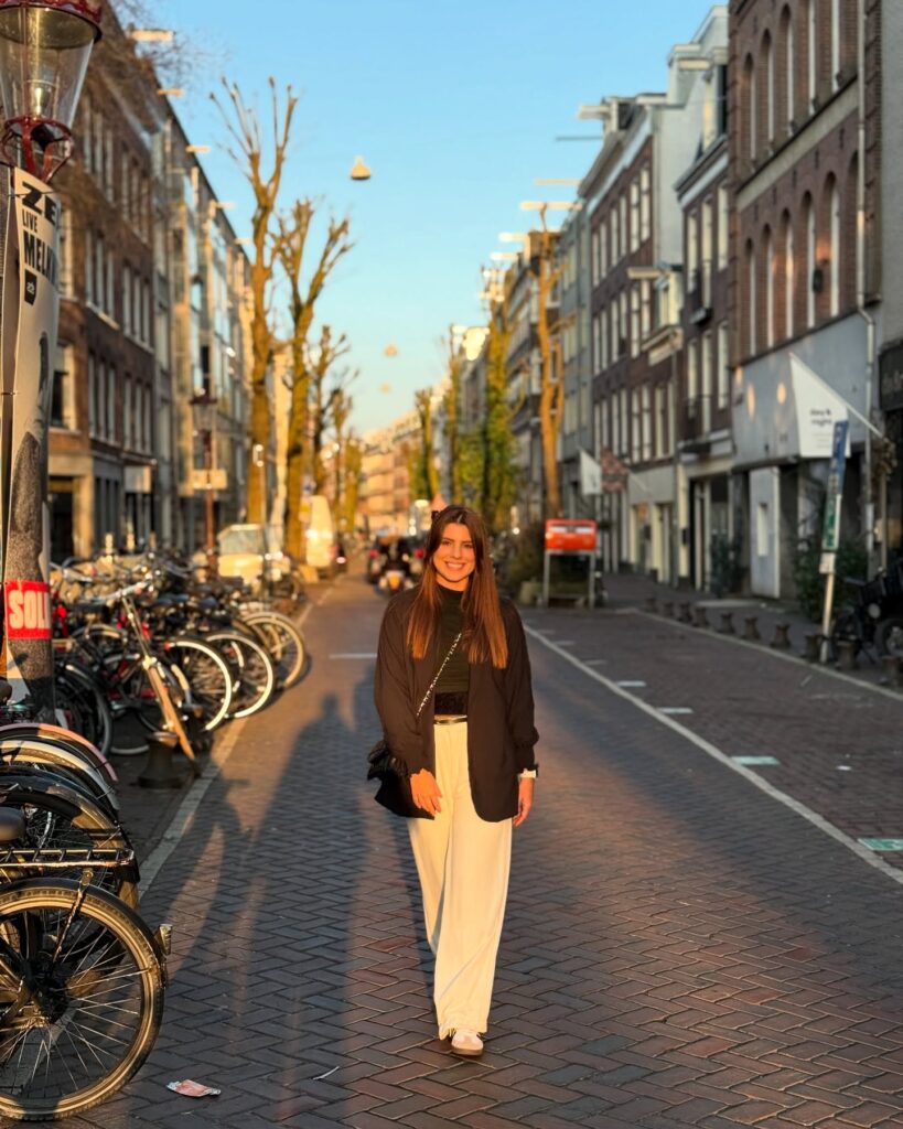 Young woman walking on a charming Amsterdam street, surrounded by bicycles, in the warm glow of sunset.