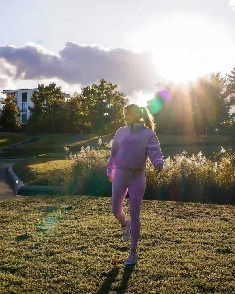Woman jogging in a purple athletic outfit during sunset in a serene park setting with lush greenery.
