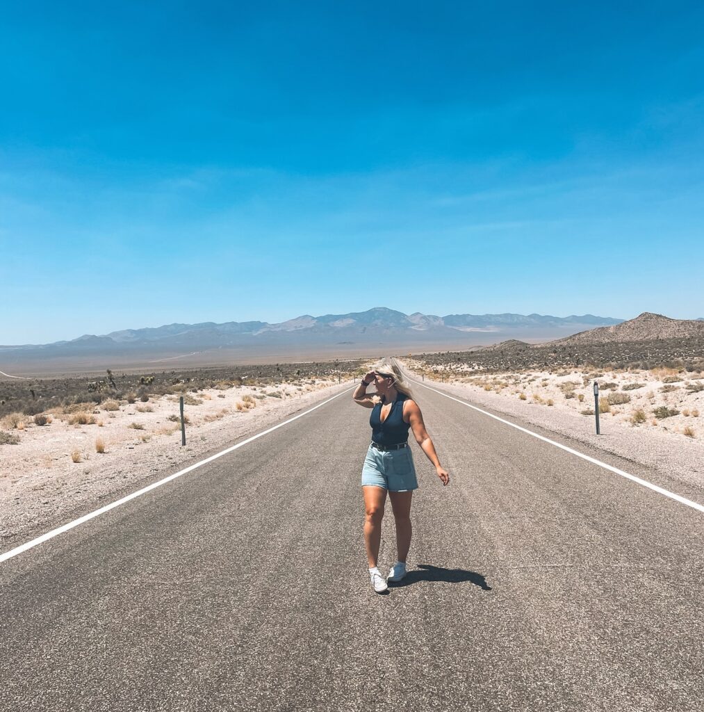 Woman walking on a deserted road under a clear blue sky with mountains in the background, enjoying the open landscape.