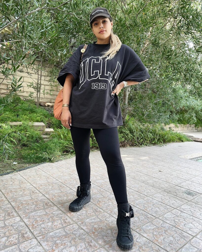 Casual outfit featuring a UCLA oversized shirt, leggings, and stylish black boots in a natural outdoor setting.