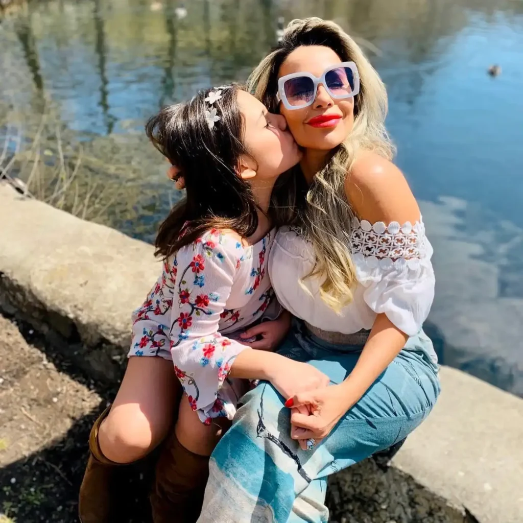 A mother and daughter share a sweet moment by the water, smiling and enjoying a beautiful sunny day together.