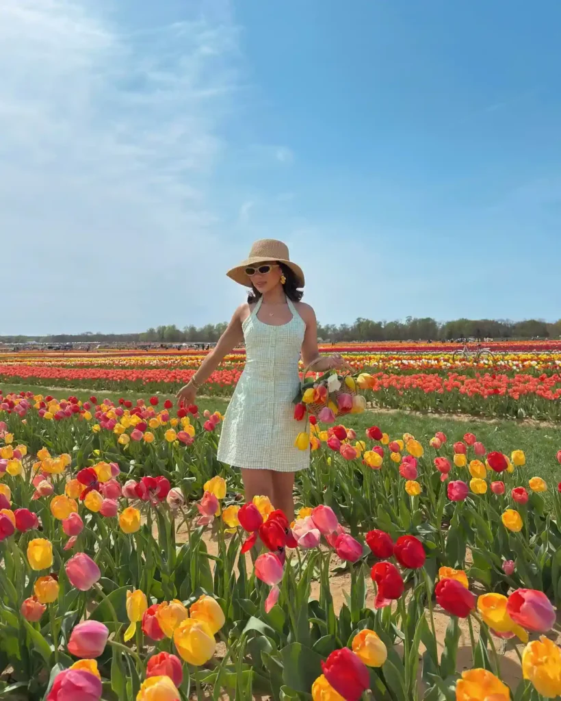 Woman in a sun hat and sundress standing in a vibrant tulip field, holding a bouquet of colorful flowers.