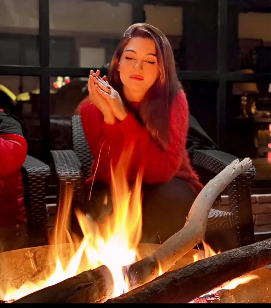 Young woman in a cozy red sweater sitting by a warm campfire, enjoying a peaceful evening outdoors.