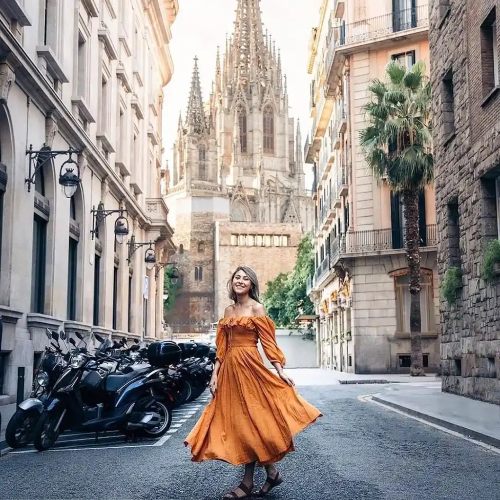 Woman in an orange dress joyfully poses on a street in Barcelona with a stunning cathedral in the background.