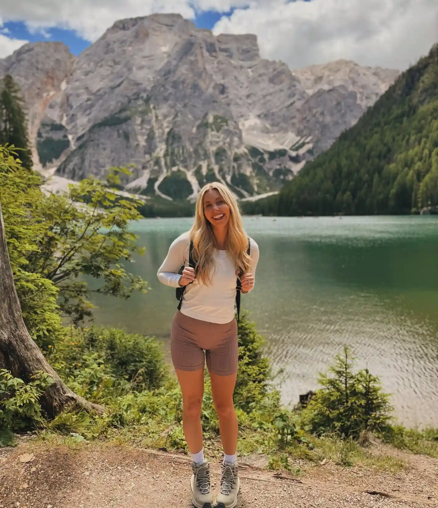 Young woman smiling by a tranquil lake with mountains in the background, ready for an outdoor adventure.