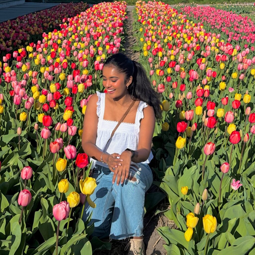 A woman smiles among vibrant tulips in a colorful flower field, enjoying a sunny day outdoors in spring.
