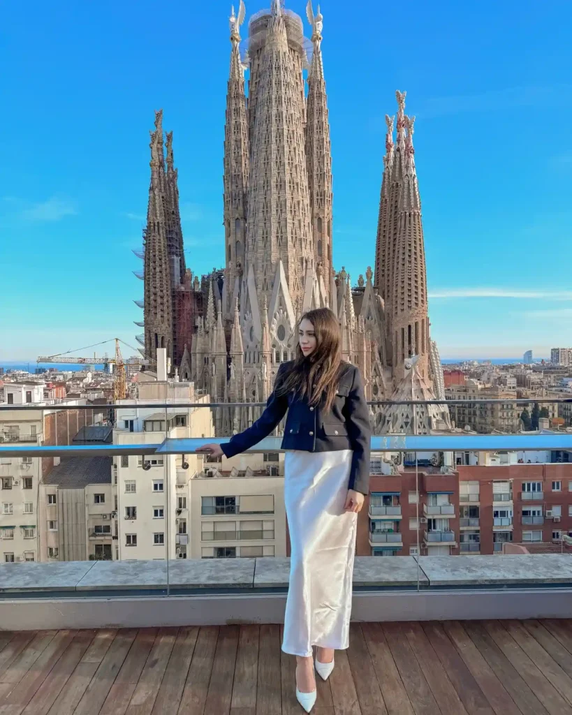 Stylish woman poses in front of Barcelona's iconic Sagrada Familia, showcasing stunning architecture and city views.