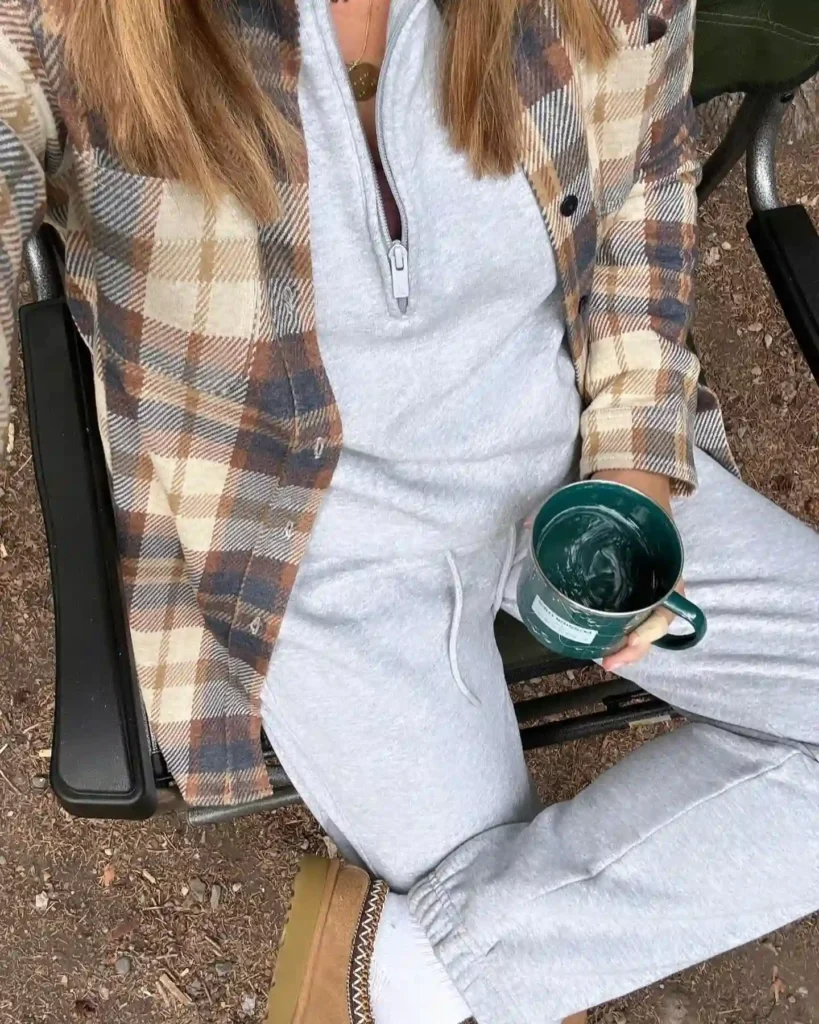 Cozy outdoor outfit featuring a plaid shirt, gray jumpsuit, and holding a green mug while sitting on a chair.