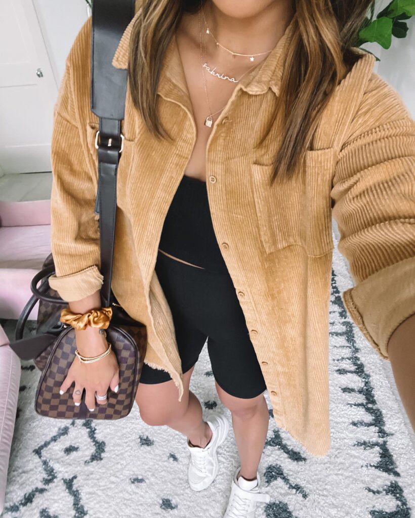 Woman in a corduroy shirt and black outfit, accessorized with jewelry and a stylish handbag in a cozy space.
