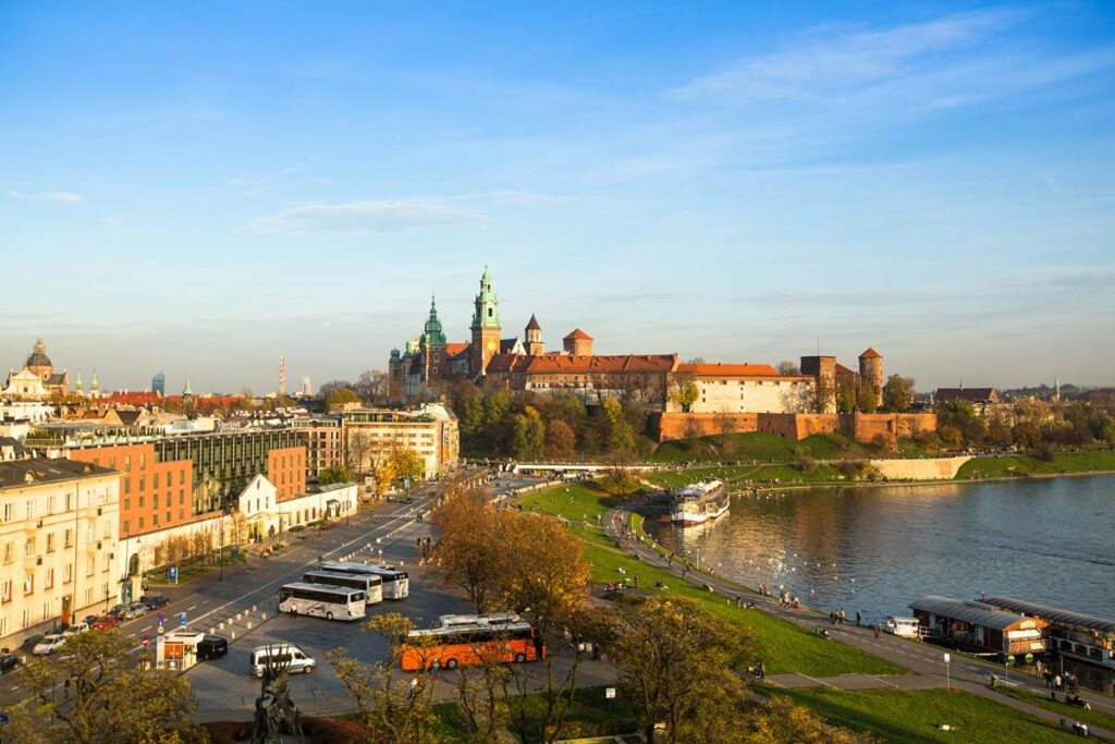 Krakow's Wawel Castle by the Vistula River on a sunny day, with vibrant autumn trees and cityscape in the background.