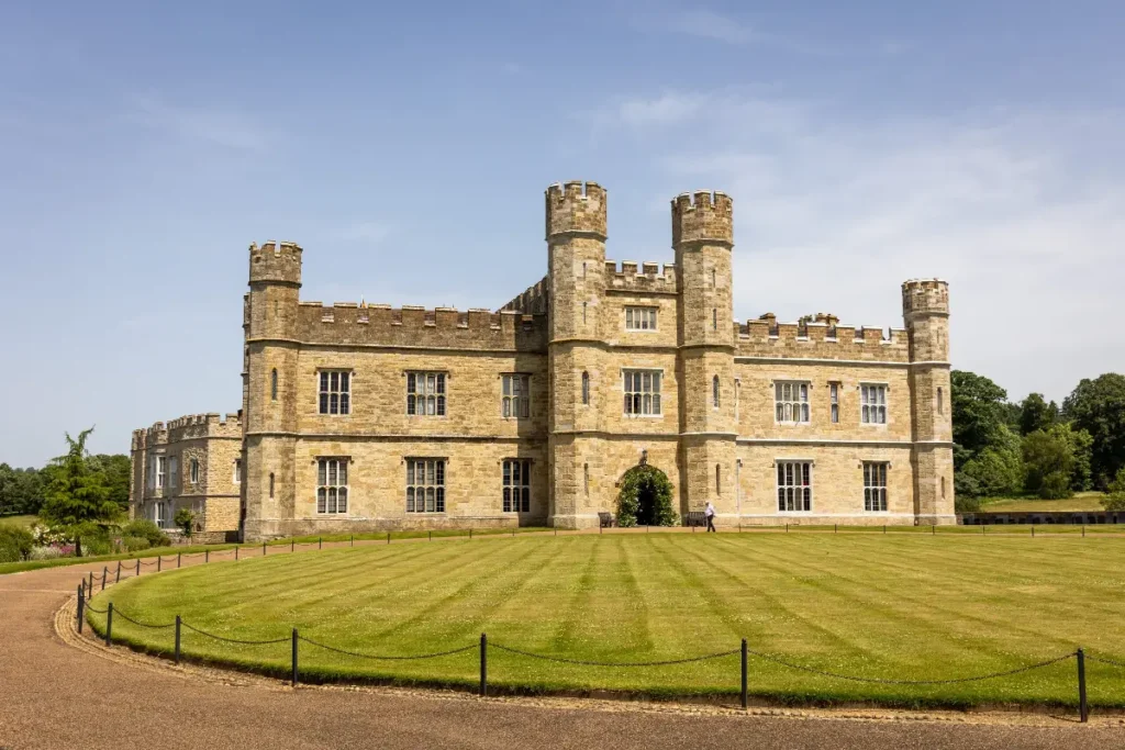 Historic stone castle with towers, surrounded by lush lawns and fencing, under a clear blue sky. Perfect for events.