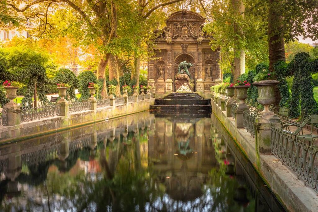 Luxembourg Gardens Medici Fountain with reflection, surrounded by lush greenery in a serene park setting.