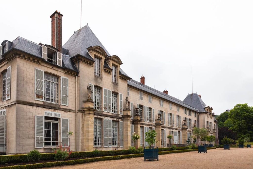 Historic French chateau with classic architecture, featuring dormer windows and manicured gardens on an overcast day.