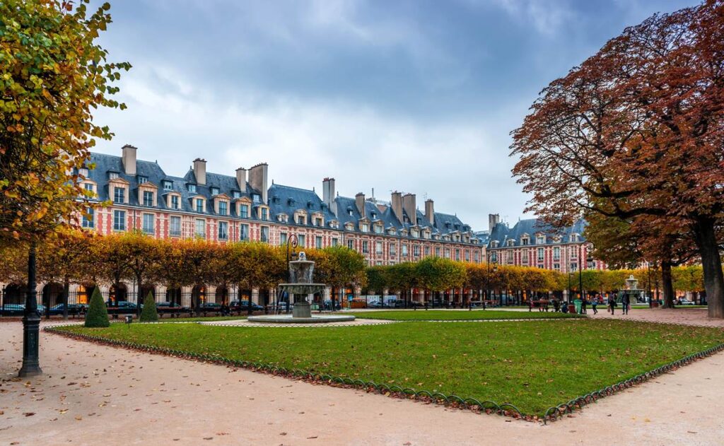 Historic Place des Vosges in Paris with autumn trees and symmetrical architecture under a cloudy sky.