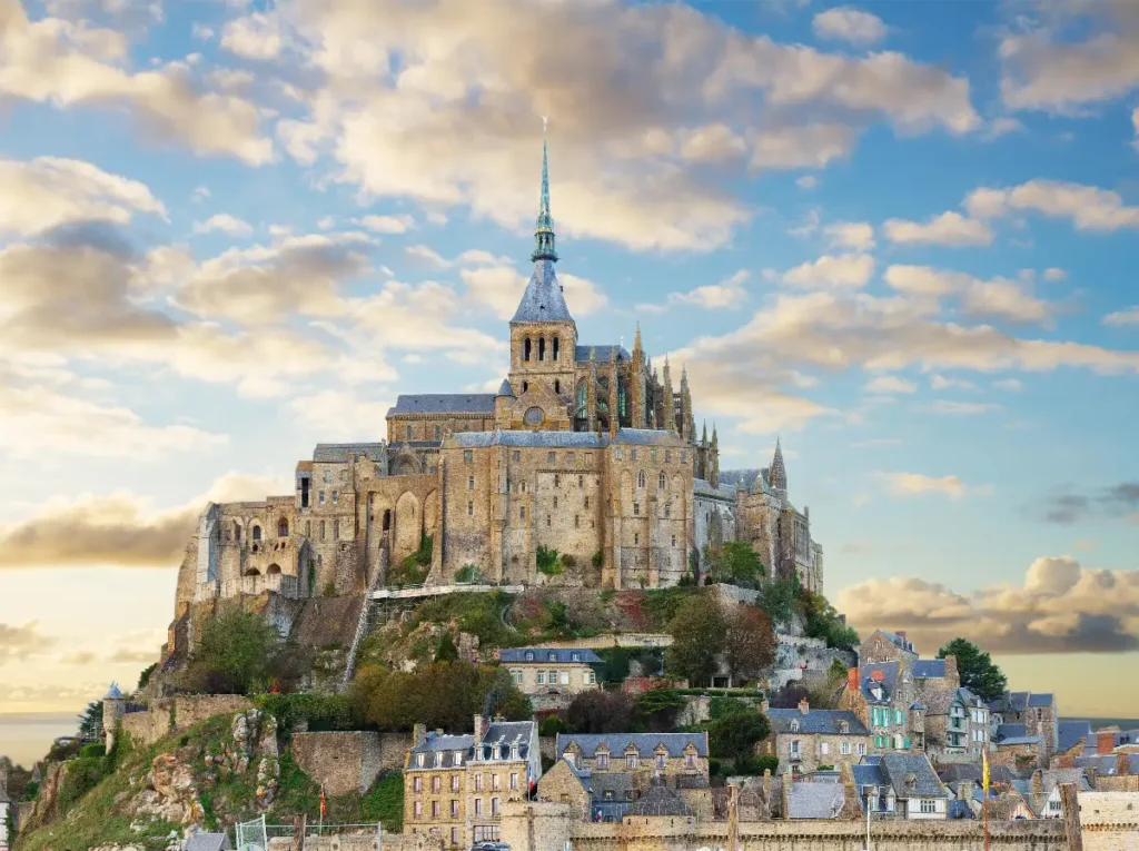 Mont Saint-Michel nestled among clouds, featuring medieval architecture and beautiful coastal scenery. Ideal travel destination.
