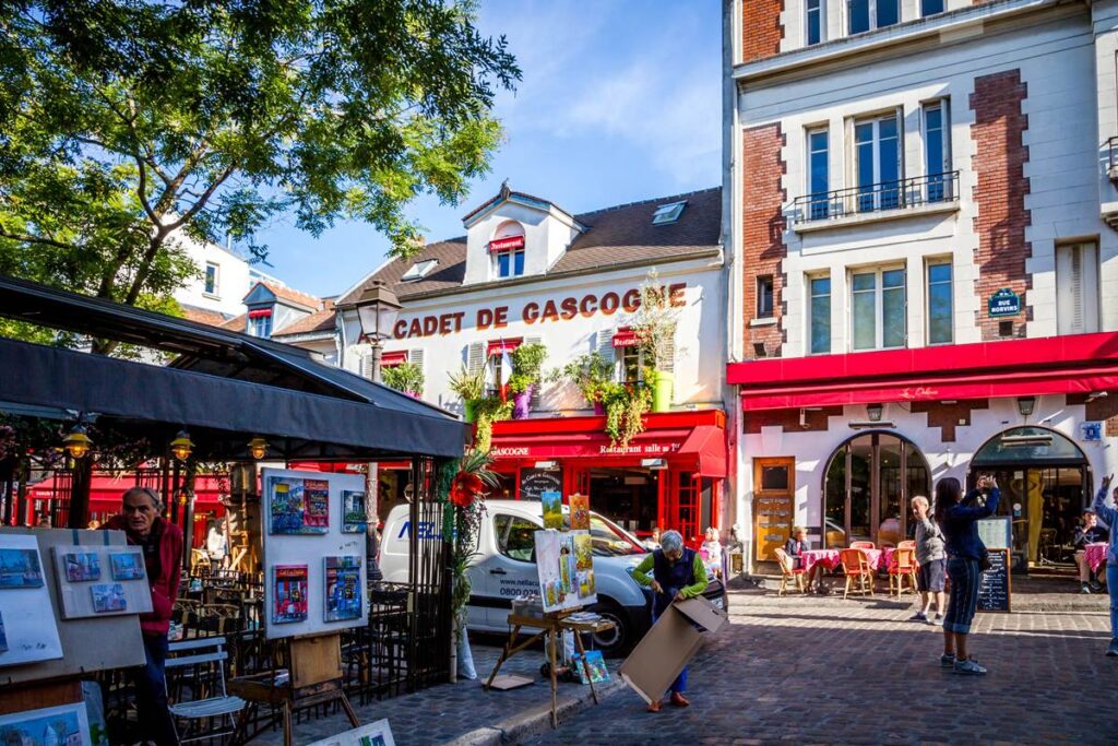 Charming Paris street scene with bright café and art displays under sunny skies on a bustling day.