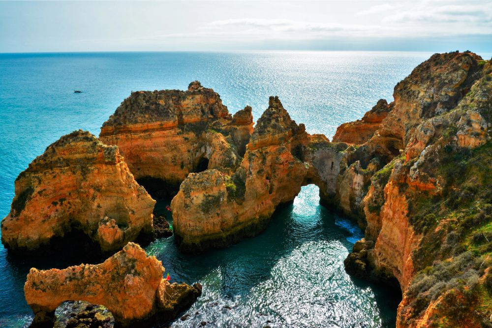 Rocky coastline under a blue sky with sparkling waters, showcasing unique rock formations along the shore.