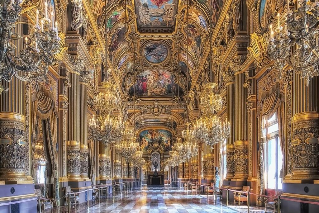 Ornate interior of a grand hall with chandeliers and intricate ceiling paintings, featuring gilded columns and rich decor.