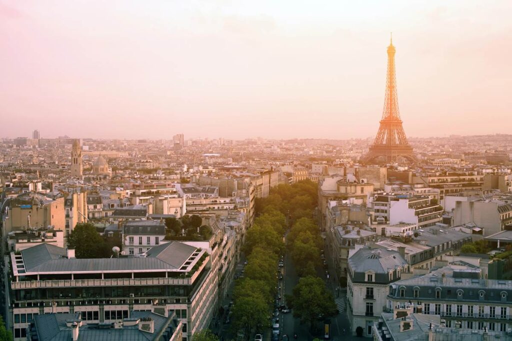 Aerial view of Paris skyline and Eiffel Tower at sunset, with tree-lined streets and historic architecture.