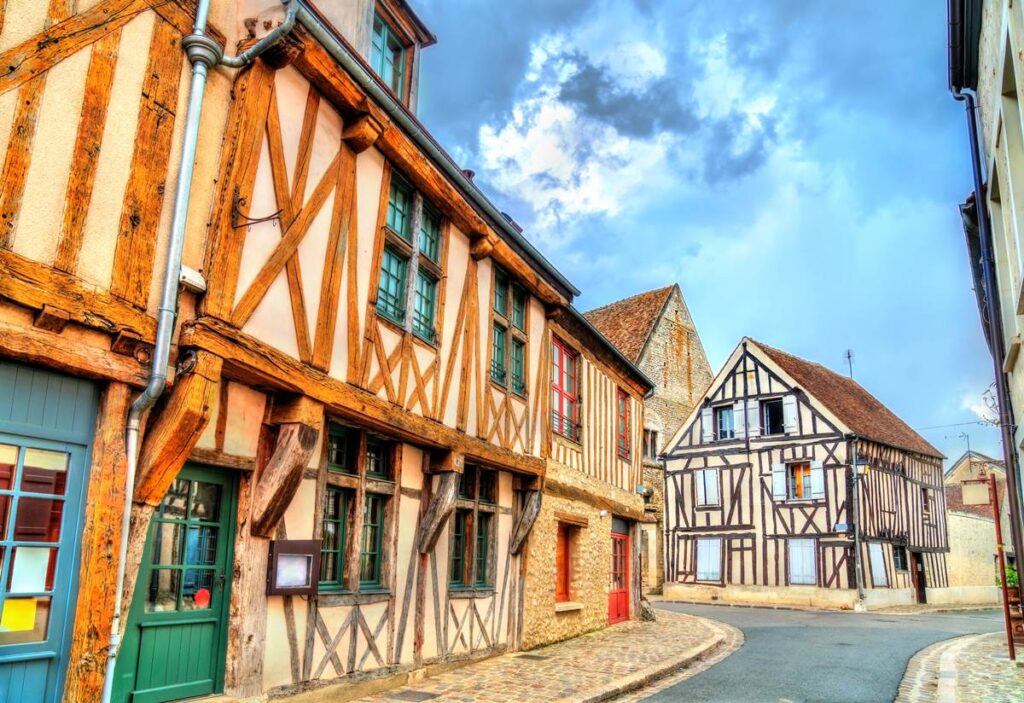 Charming medieval timber-framed houses in a quaint European village with cobblestone streets under a cloudy sky.