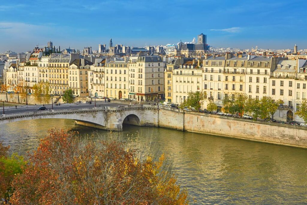 Parisian river scene with historic architecture, bridge over the Seine, and autumn trees under a clear sky.