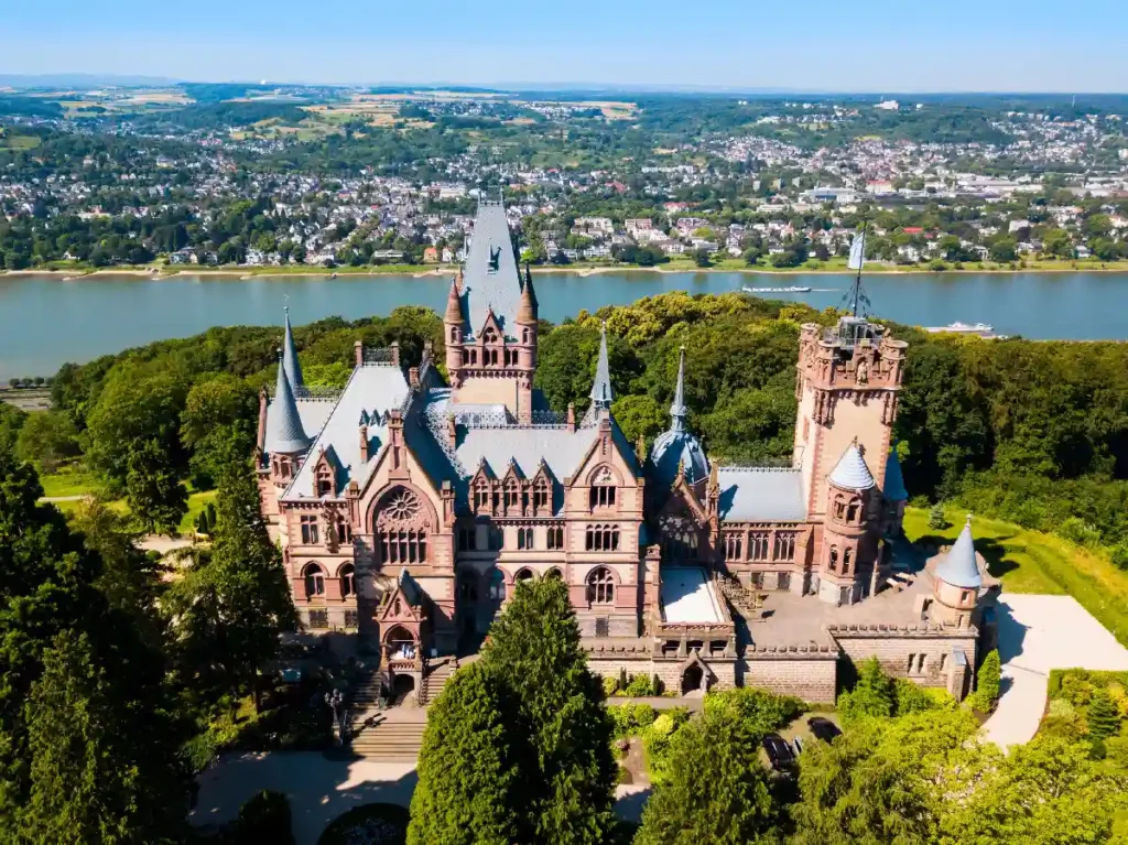 Stunning aerial view of a historic castle surrounded by lush greenery and a river, showcasing beautiful architecture.
