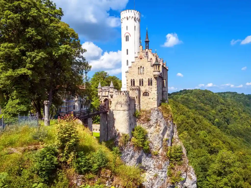 Stunning view of a medieval castle perched on a rocky cliff surrounded by lush greenery and blue skies.